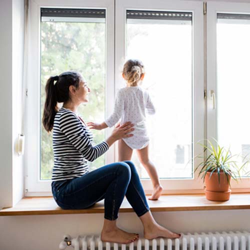 Mom and young daughter standing in front of a large window during summer | Cooling Services