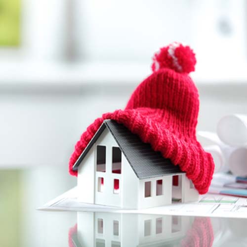 Red winter tossle hat sitting on top of a model of house | Heating Services